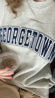 a woman is holding a plastic container with food in it while wearing a georgetown shirt