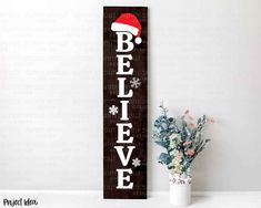 a wooden sign that says believe with a santa hat on it next to a potted plant