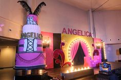 a large pink cake sitting on top of a counter next to a sign that says angellica