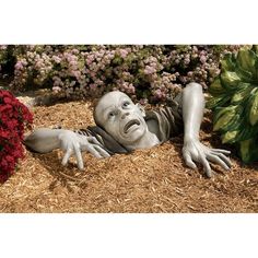 a statue of a person laying on the ground in front of some flowers and grass