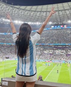 a woman standing in front of a crowd at a soccer game with her arms up