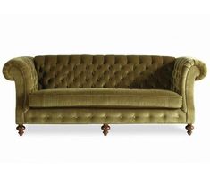 a green velvet couch with wooden legs and buttons on the back, sitting in front of a white background