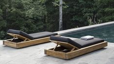 two chaise lounges sitting next to a pool with trees in the back ground