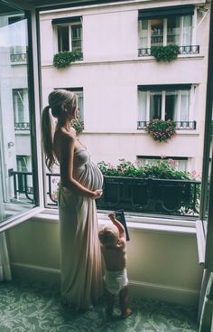 a woman standing next to a child near a window