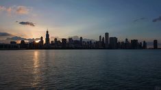 the sun is setting over the city skyline as seen from across the water on a cloudy day