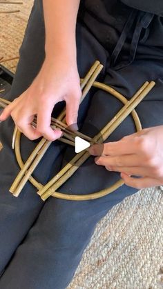 a person sitting on the floor with some sticks in front of her and one hand holding something