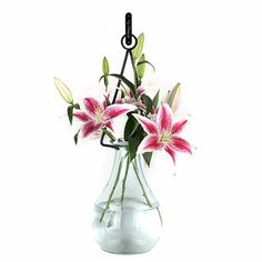 a glass vase filled with pink and white flowers on top of a table next to a metal hook