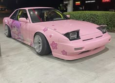 a pink car with flowers painted on the front and side, parked in a parking lot