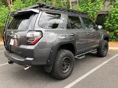 a gray four door suv parked in a parking lot next to some bushes and trees