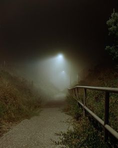 a foggy night with street lights on the side of a road and grass in the foreground