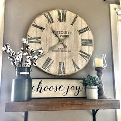 a clock that is on the wall above a shelf with flowers and candles in vases