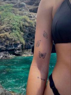 a woman with a butterfly tattoo on her arm next to the ocean and rocks in the water