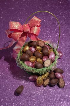 a basket filled with lots of chocolates next to a pink bow on top of a purple surface