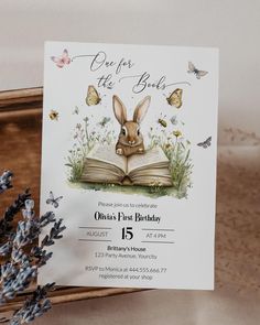 an open book with a rabbit on it and butterflies around it is sitting next to some lavenders