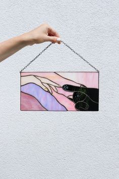 a hand holding a piece of art hanging from a chain on a wall with the image of two hands touching each other