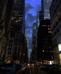 an empty city street at night with tall buildings in the background and cars parked on the side