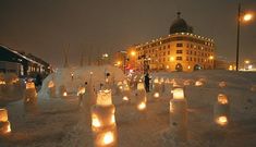 many lit candles are placed in the snow near a building and street lights at night