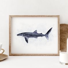 a painting of a shark is displayed in a frame next to a cup and basket