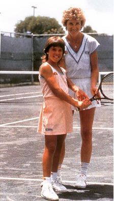 two women standing on a tennis court holding racquets and posing for the camera