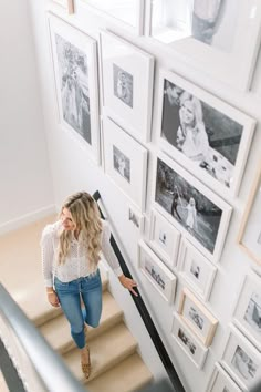 a woman is walking down the stairs in front of many framed pictures on the wall