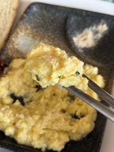 a spoon with some food in it on a black plate next to a piece of bread