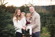 a man and woman holding two children in front of a christmas tree stand at sunset