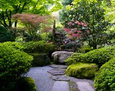 a stone path surrounded by green trees and rocks in a garden with moss growing on the ground