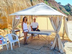 a man and woman standing under a tent on the beach