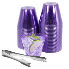 purple plastic cups with limes and ice in them next to a cocktail shaker