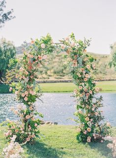 an outdoor wedding ceremony with flowers and greenery on the side of the water's edge