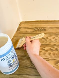 a person holding a paintbrush next to a cup of tea on a wooden table