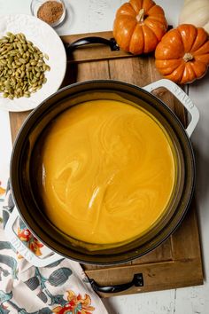 a pot filled with yellow liquid sitting on top of a wooden cutting board next to pumpkins