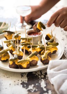 a plate full of food with pickles on skewers and cheese sauce being drizzled over them