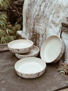 three white dishes sitting on top of a table next to an old brick wall and planter