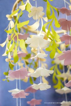 a close up of a mobile made out of paper flowers and leaves on a blue background