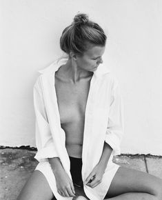 a black and white photo of a woman sitting on the ground with her shirt open