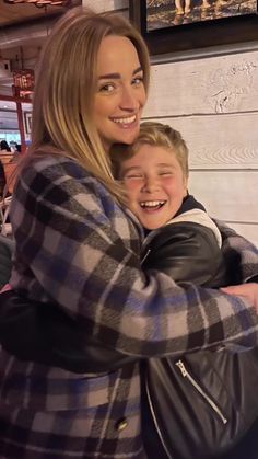 a woman hugging a boy in front of a wooden wall with pictures on the wall