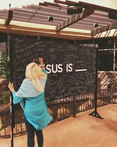 a woman writing on the side of a blackboard with jesus is written on it