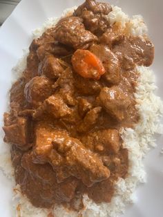 a white plate topped with rice and meat covered in gravy on top of it