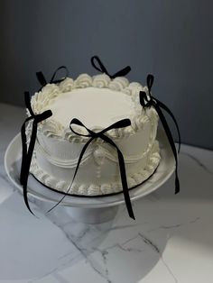 a white cake sitting on top of a marble plate covered in black ribbon and bow