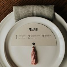 a white plate topped with a menu and a tasseled piece of paper on top of it