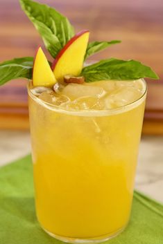 a glass filled with orange juice and topped with an apple garnished with leaves