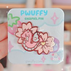 a person holding up a pink enamel pin with flowers in the shape of an elephant