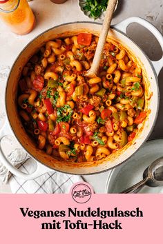 a pot filled with pasta and vegetables on top of a white table next to utensils