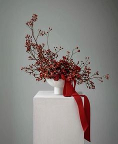 a vase filled with red flowers on top of a white table next to a gray wall