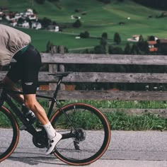 a man riding a bike down a street next to a wooden fence and green hills