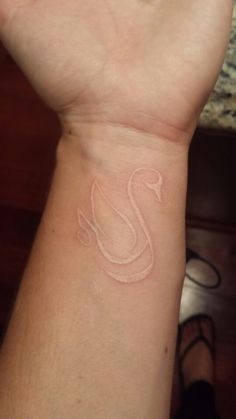 a person's arm with a small white swan tattoo on the left side of their wrist