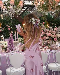 a woman in a pink dress standing next to a table with white chairs and flowers