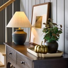 a table with a lamp and pictures on it next to a stair case in a house