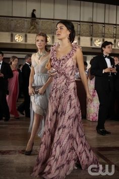 two women dressed in evening gowns walking through a hall